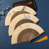 Open bamboo folding hand fan with yellow paper surface showing a painted crane design and a brown tassel