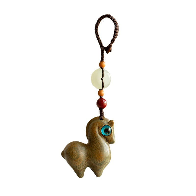 Close up of a bronze colored horse keychain with a green eye and jade bead