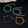 Four colorful woven bracelets with gold-tone beads and bells displayed on a dark surface