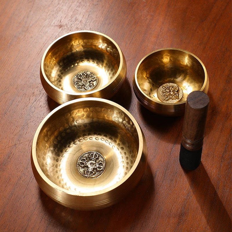 Three gold-tone copper singing bowls with wooden strikers on a dark wood table