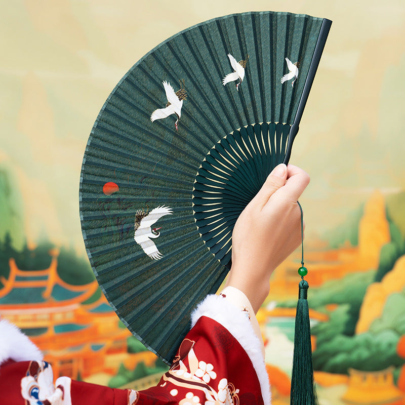 Hand holding a dark green vintage folding fan with white crane designs