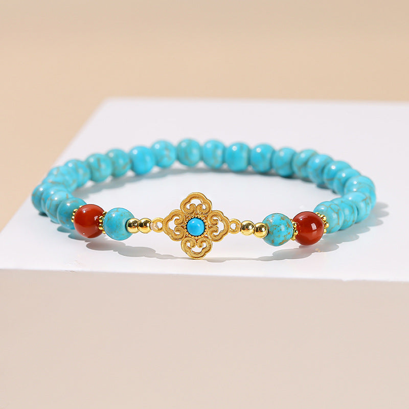 Close up of a blue turquoise beaded bracelet with a gold Ruyi charm on a woman's wrist