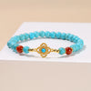 Close up of a blue turquoise beaded bracelet with a gold Ruyi charm on a woman's wrist