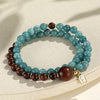 A wrist wearing a double wrap bracelet with blue chalcedony and dark wood beads and a small gold charm