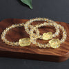 A natural citrine beaded bracelet with a carved Pixiu charm resting on a wooden surface.