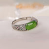 A silver-tone open ring with a green oval stone and decorative side details