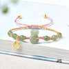 Wrist wearing a green jade rabbit bracelet with red string and gold accents