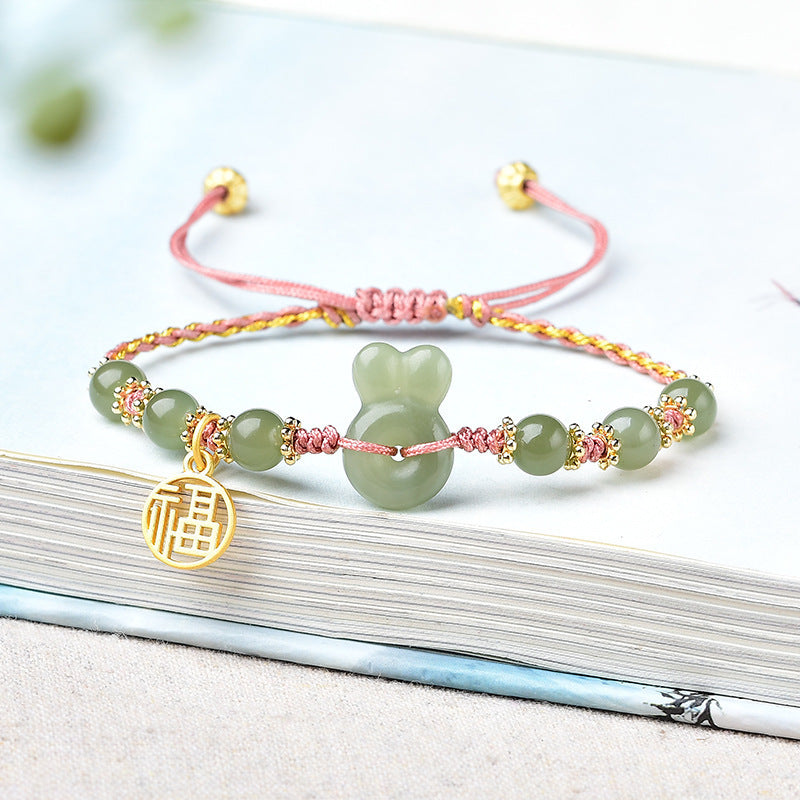 Wrist wearing a green jade rabbit bracelet with red string and gold accents
