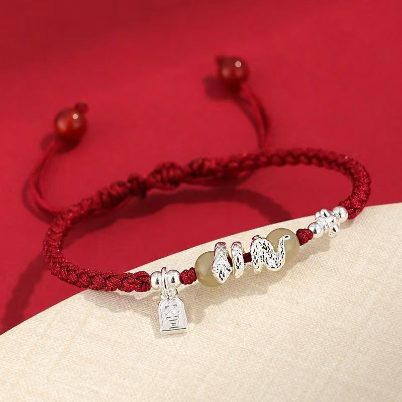 Close-up of a red braided bracelet with a silver snake charm and bead accents