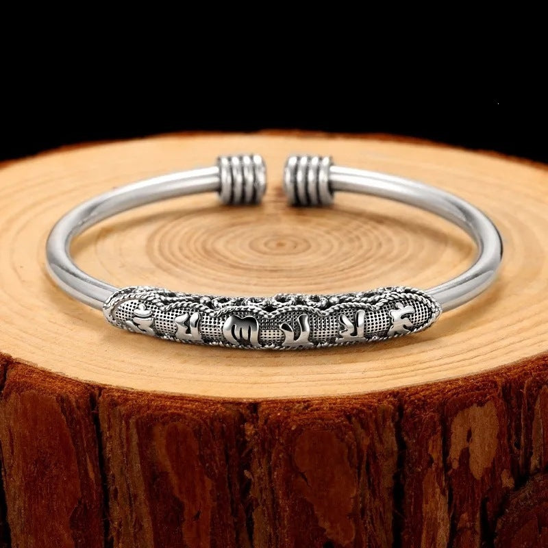 Silver tone open cuff bracelet with engraved Om Mani Padme Hum mantra on a wooden surface