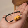 Close-up of a black braided bracelet with a yellow carved bear charm held in a hand