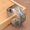 Silver tone wide cuff bracelet with hollow lotus flower pattern on a wooden background