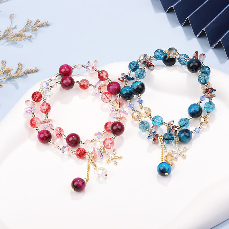 Double wrap tiger eye bracelet with red beads and gold flower charm on white surface