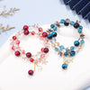 Double wrap tiger eye bracelet with red beads and gold flower charm on white surface