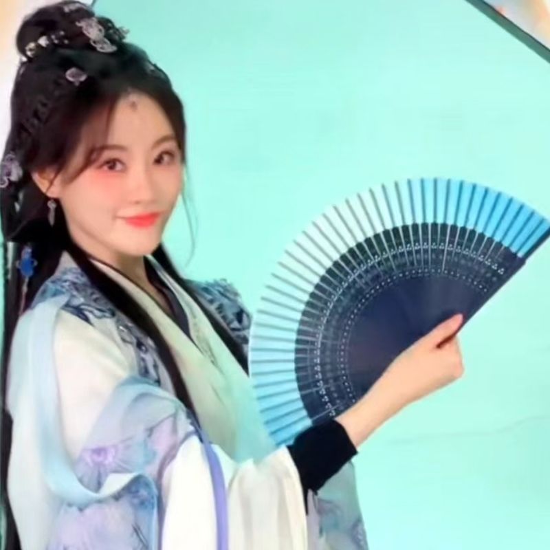 A woman holding a blue gradient folding fan with a tassel
