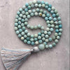 Coiled light blue natural stone mala necklace with a multicolor tassel on a grey background