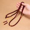 Coiled red blood amber 108 bead mala necklace with yellow cord on a beige background
