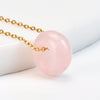 Close up of a pink rose quartz donut pendant on a gold chain