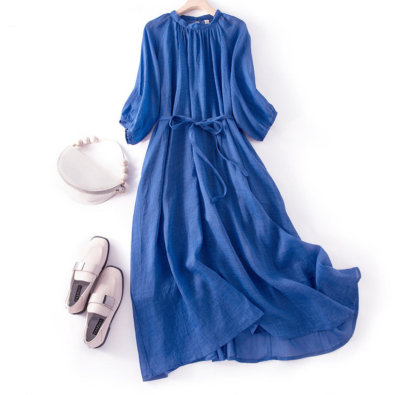 Flat lay of a blue cotton linen long dress with flutter sleeves and a tie waist on a white background