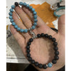 Two beaded bracelets held in a hand, one white and one black, connected by silver crown charms