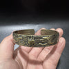 Hand holding an antique brass copper cuff bracelet with dragon and phoenix relief carving