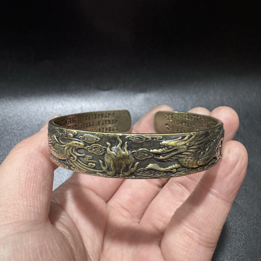 Hand holding an antique brass copper cuff bracelet with dragon and phoenix relief carving