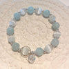 Light blue and white cat's eye bead bracelet with a silver butterfly charm on a woven mat