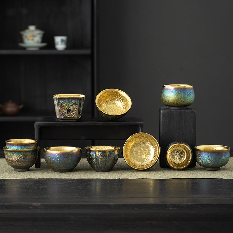 A collection of colorful ceramic teacups with gold interiors arranged on black blocks.