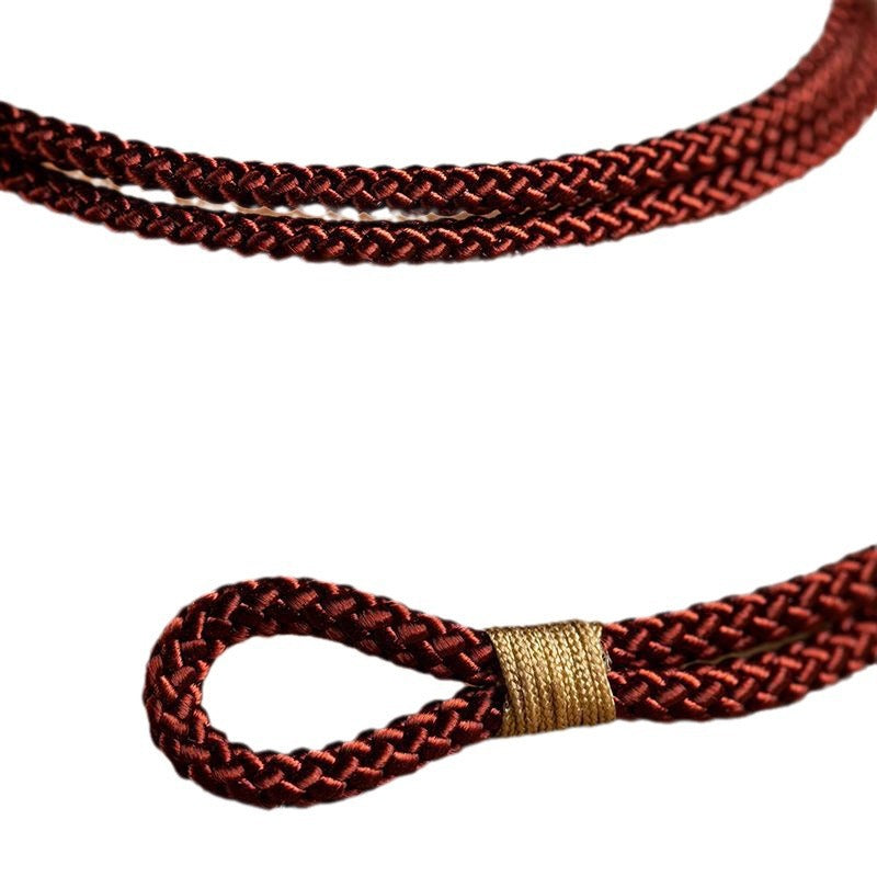 Close-up of a braided red string bracelet with a gold tone button clasp