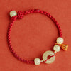 Close-up of a red braided bracelet with a white peace buckle and gold-tone lotus pod charm