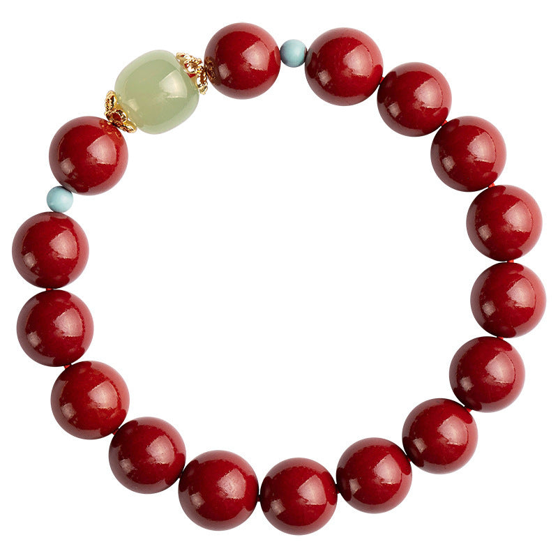 A circular bracelet made of round red cinnabar beads with one light green jade bead and gold accents.