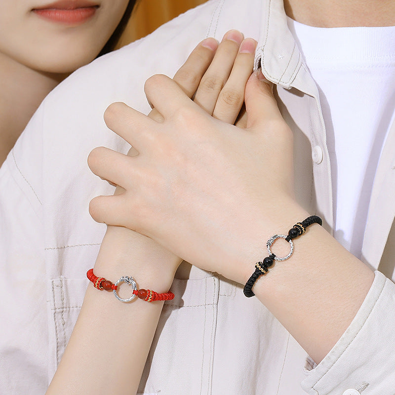 Two hands wearing red and black braided bracelets with silver rings