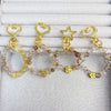 Four crystal beaded keychains with gold-tone heart and star clasps lying on white fabric