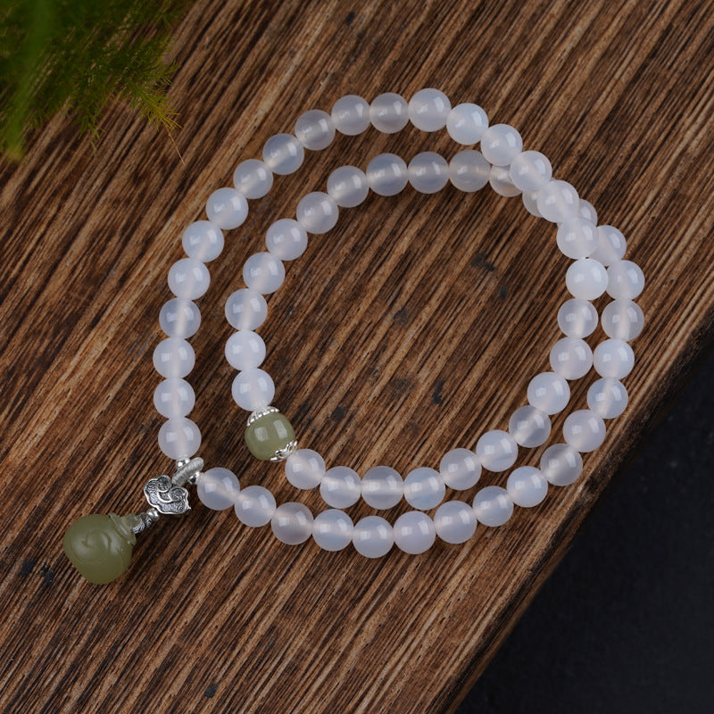White agate beaded bracelet with a green jade drop charm on a wooden surface