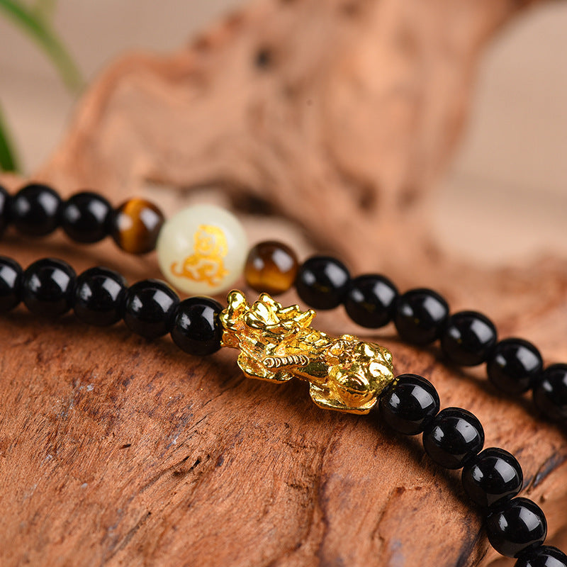 Coiled black obsidian mala bracelet with gold Pixiu charm on wood
