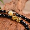 Coiled black obsidian mala bracelet with gold Pixiu charm on wood