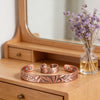 A copper cuff bracelet and ring with a rose pattern sitting on a wooden vanity table