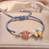 Blue braided bracelet with a peach peace buckle and gold flower charm on a beige background