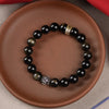 Close-up of a black and gold sheen obsidian beaded bracelet with a gold charm on a clay plate