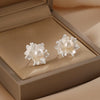 A pair of silver-tone flower stud earrings with a natural pearl center in a beige box