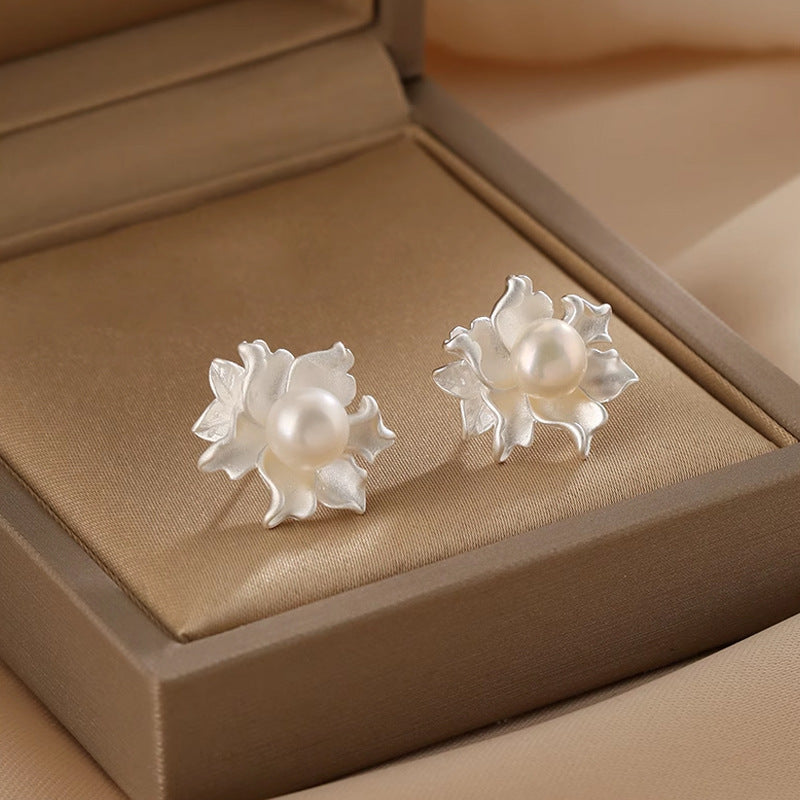 A pair of silver-tone flower stud earrings with a natural pearl center in a beige box