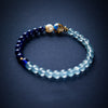 Blue beaded bracelet with a gold-tone enamel fish bead on a dark background