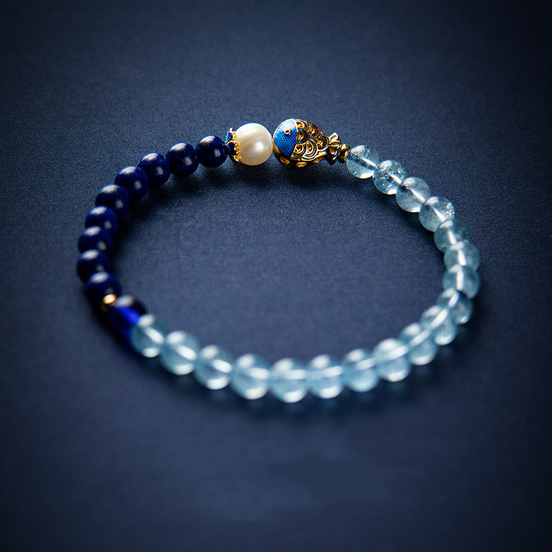 Blue beaded bracelet with a gold-tone enamel fish bead on a dark background