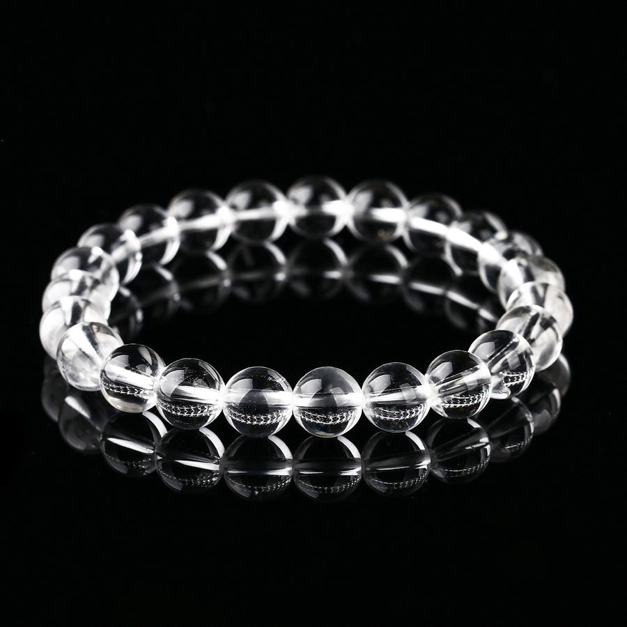 A close-up view of a clear crystal beaded bracelet on a black reflective surface