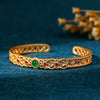 Gold tone open cuff bangle with green center stone and filigree details
