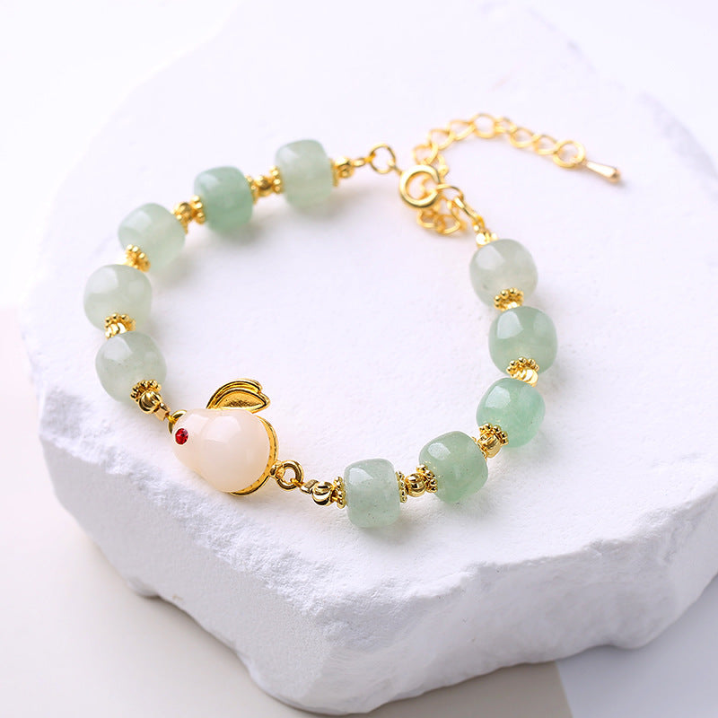Close-up of a handmade green aventurine bead bracelet with a white rabbit charm and gold-tone accents.