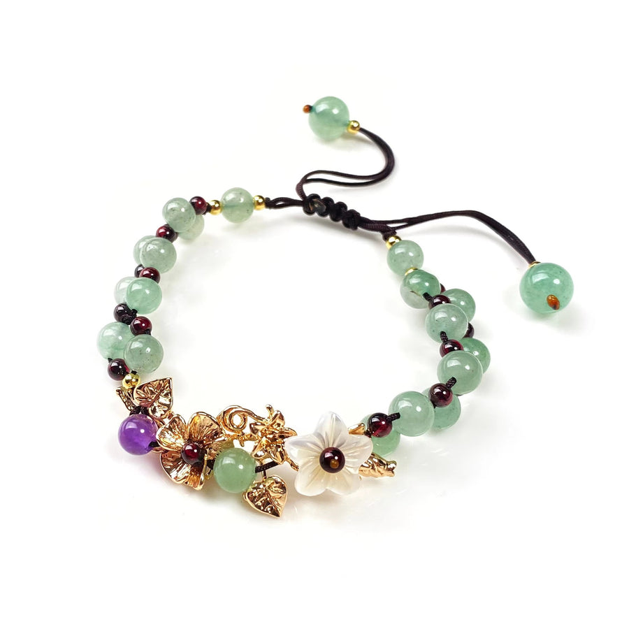 Close up of a green beaded bracelet with a gold flower charm on a white background