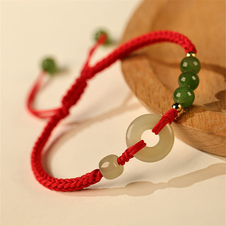 Close-up of a red string bracelet with a white jade peace buckle and green beads