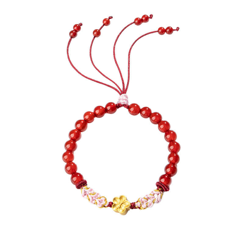 Red beaded bracelet with a gold flower charm and adjustable cord ties on a white background