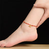 Close up of a foot wearing a red braided anklet with a gold lotus pod charm